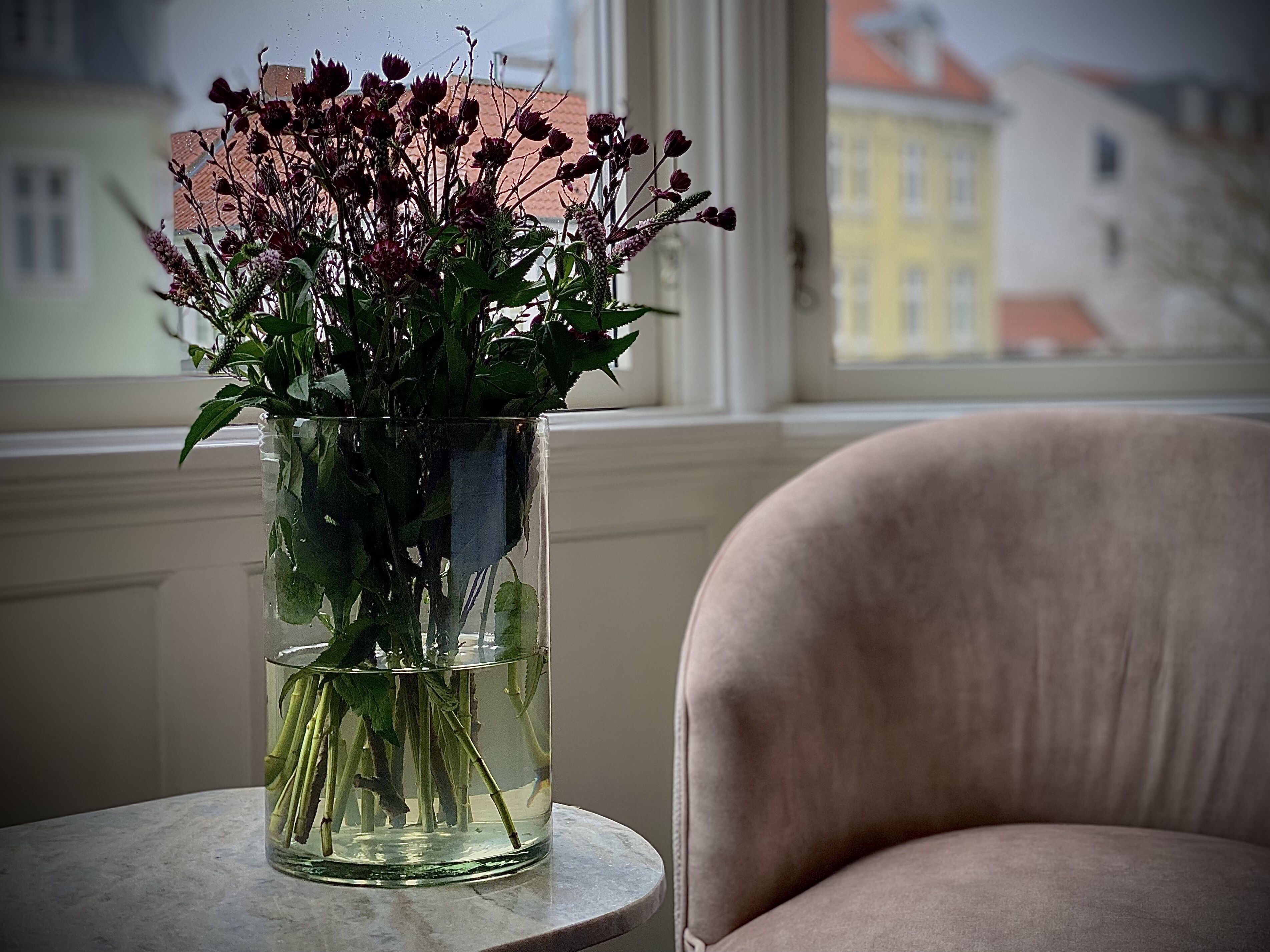 Un vase rempli de fleurs est posé sur une table près d’une fenêtre.