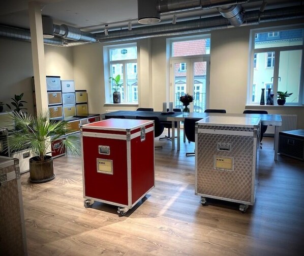 A spacious office with large windows, wooden floors, and two wheeled storage units. - Teaterhotellet (Horsens)