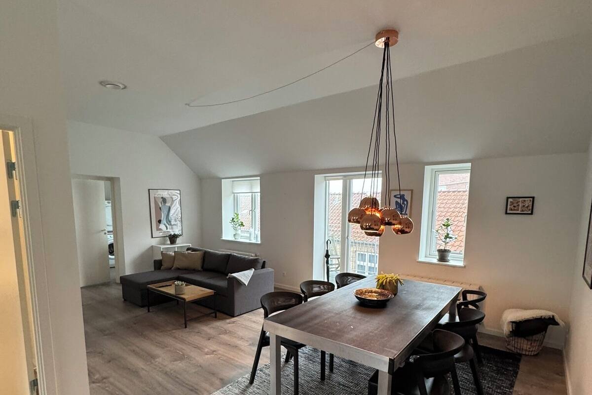 A spacious living area with a dining table, sofa, and a hanging light fixture.