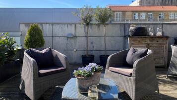 A rooftop patio with wicker furniture, a glass table, and potted plants.
