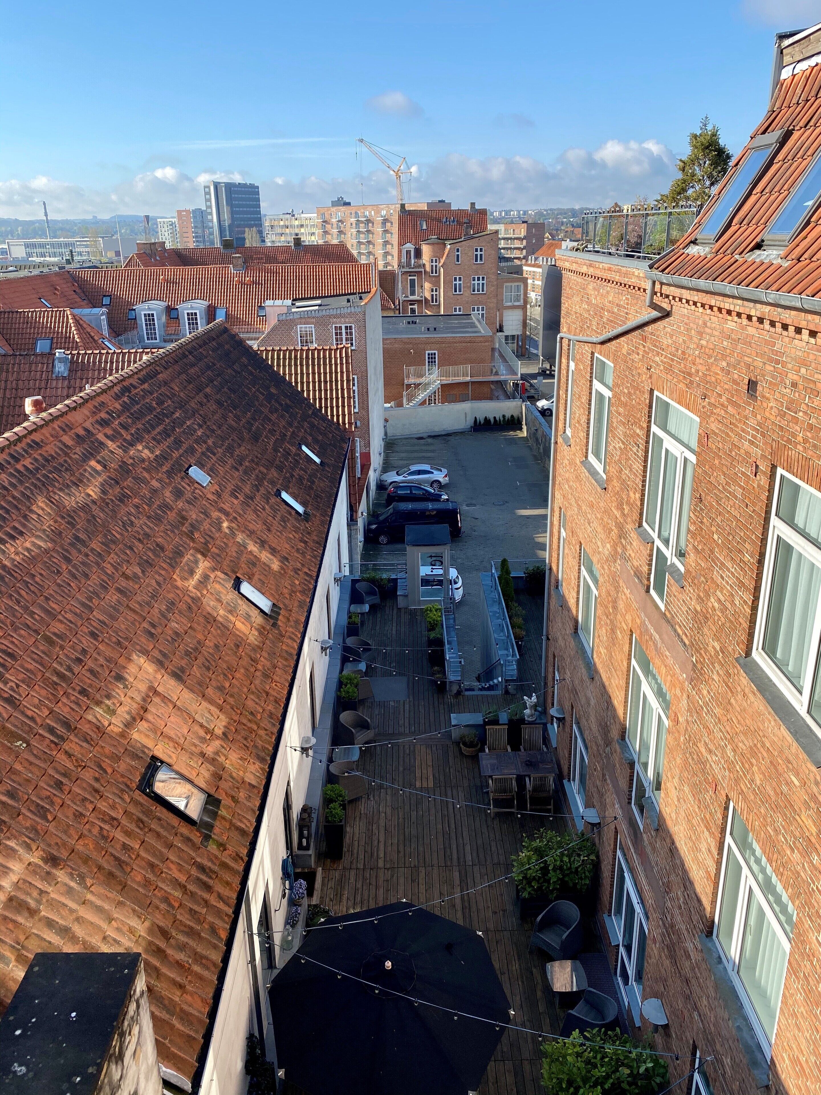 Una terraza en la azotea con vistas a la ciudad, que cuenta con un área pavimentada, mobiliario exterior y una sección cubierta.