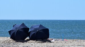 Two beach umbrellas on a sandy beach with a clear view of the ocean. - Teaterhotellet (Horsens)