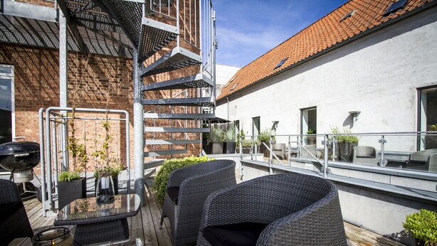 A rooftop patio with wicker furniture, a glass table, and potted plants. - Teaterhotellet (Horsens)