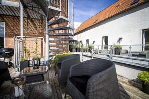 A rooftop patio with wicker furniture, a glass table, and potted plants. - Teaterhotellet (Horsens)