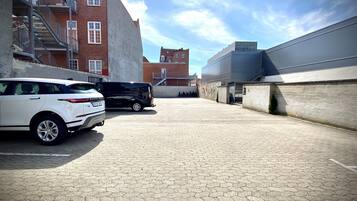 A parking area with two cars, a white SUV and a black van, adjacent to a building with a brick facade and a staircase.