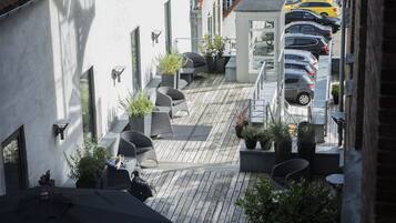 Un estrecho callejón con una terraza de madera, asientos al aire libre y plantas en macetas.