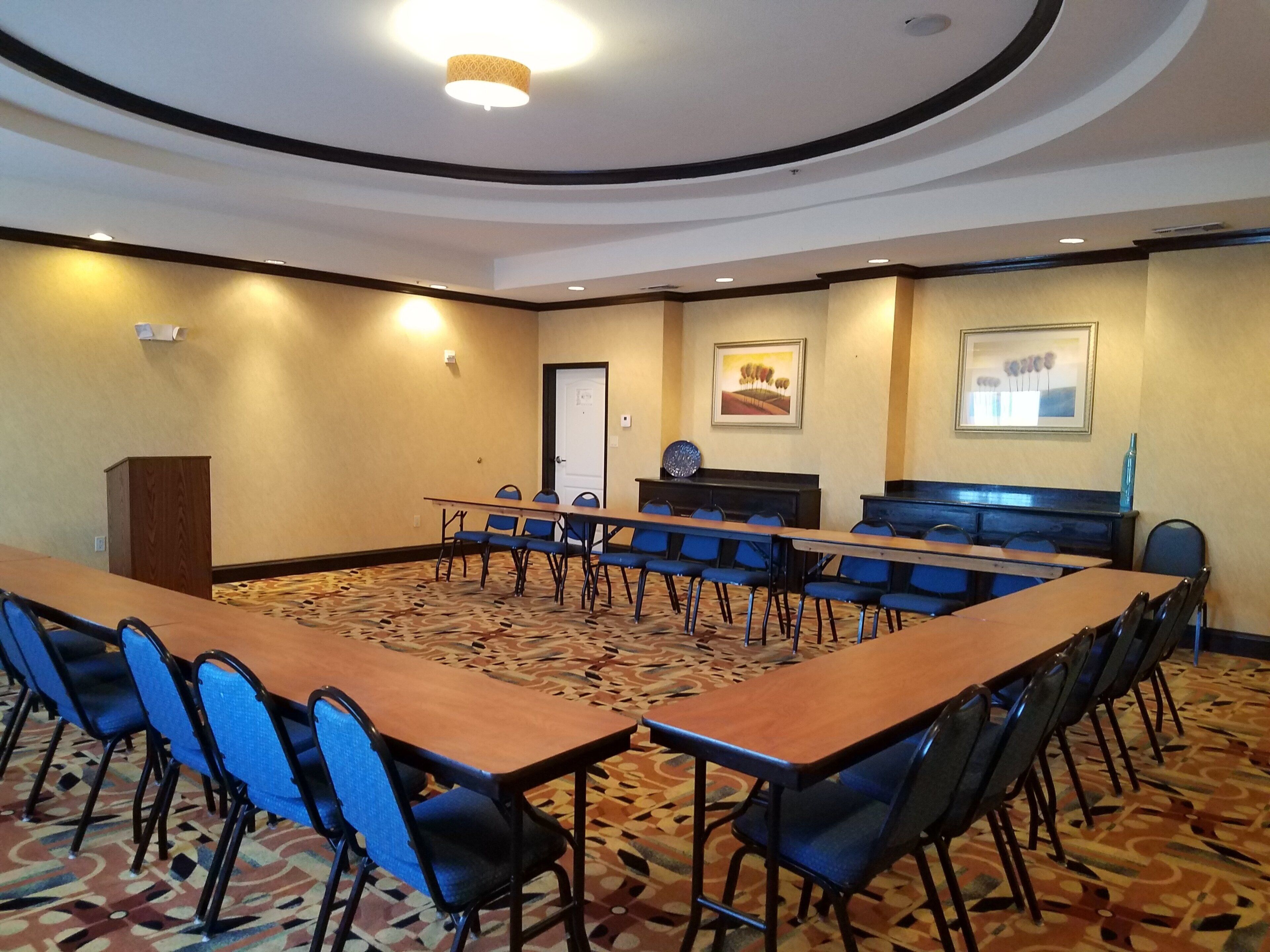 A conference room with a long table, chairs, a podium, and framed artwork on the walls.