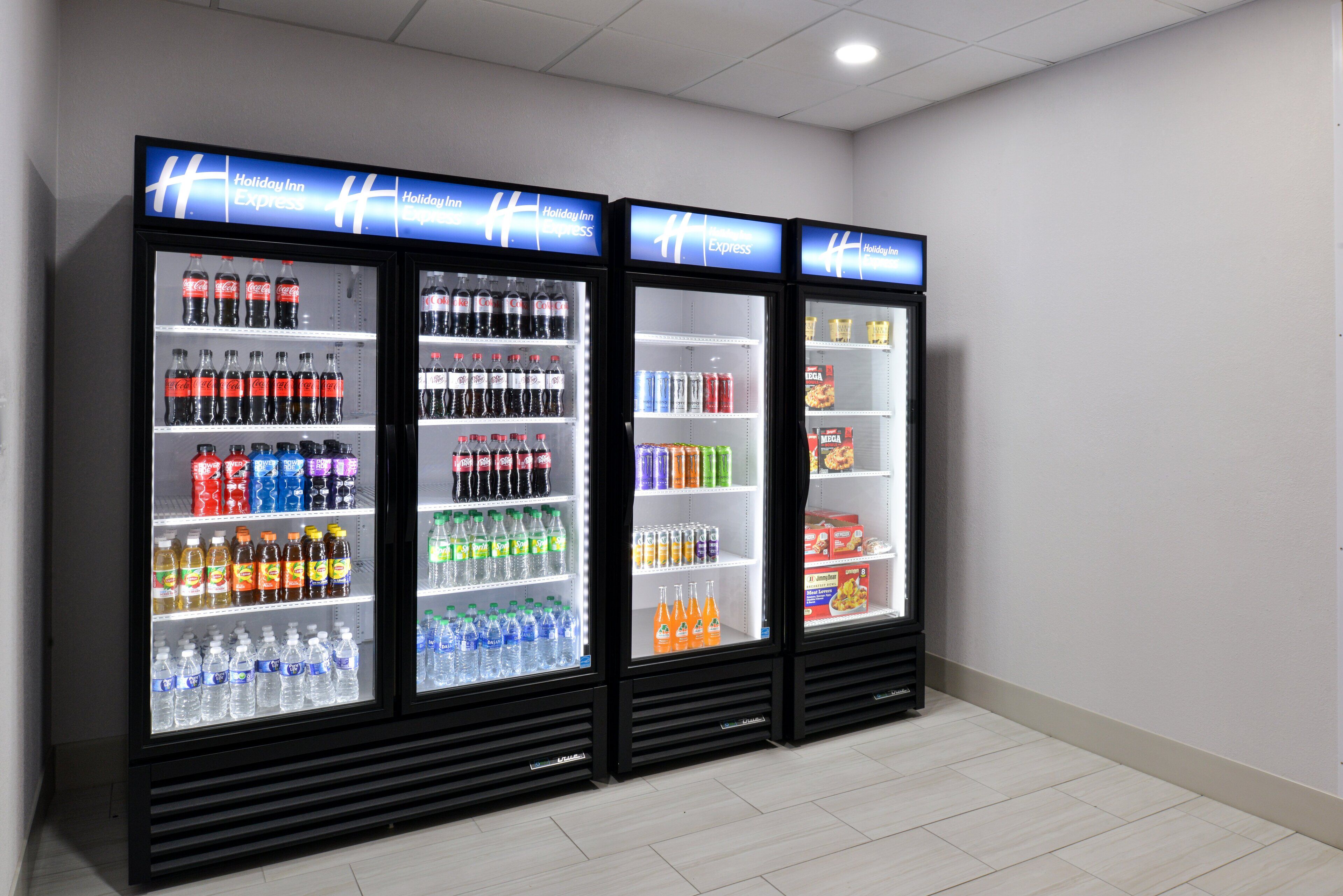 Three refrigerated display cases in a hotel lobby, each stocked with various beverages and snacks.