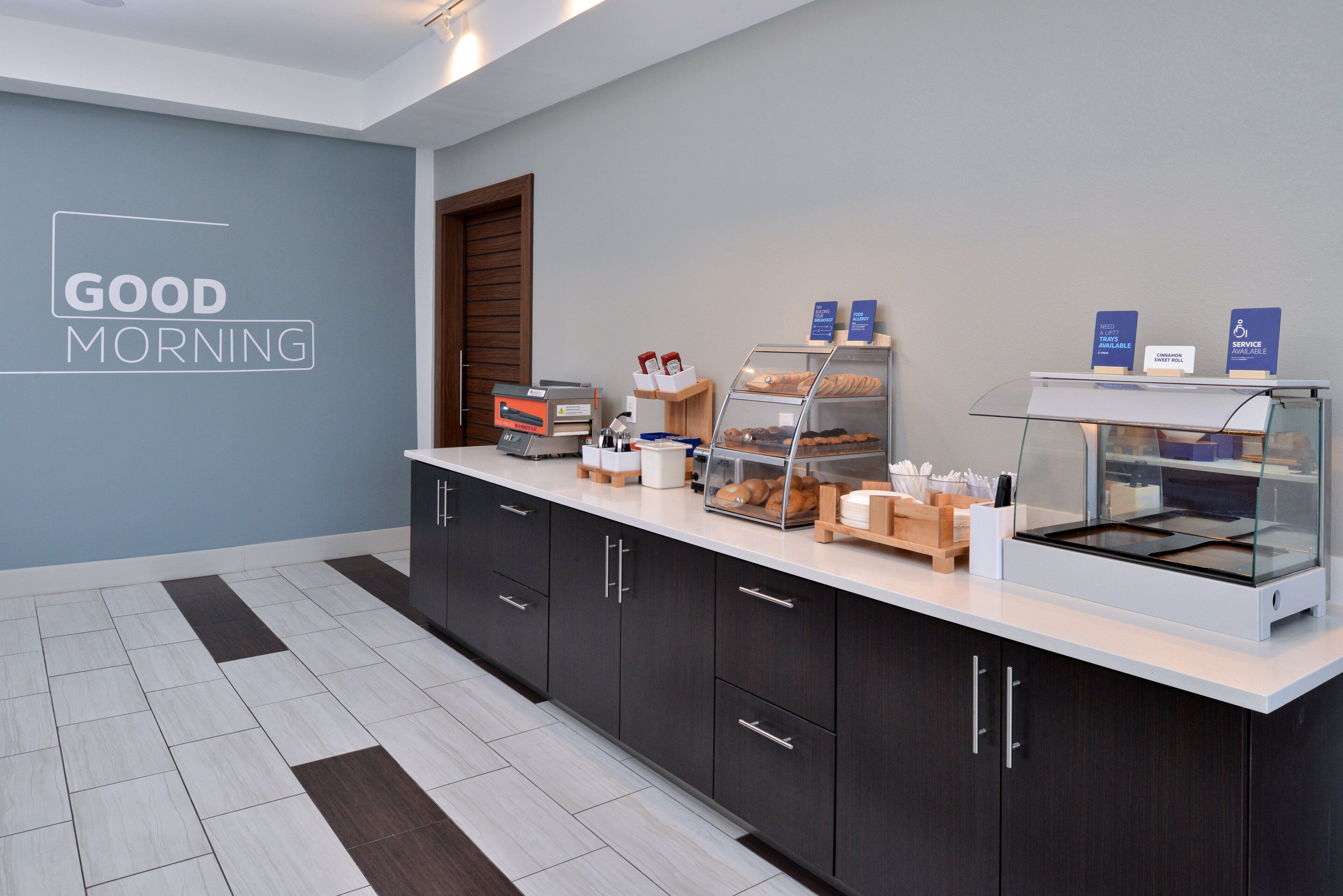 A modern breakfast area with a counter, display cases, and a wall sign reading "GOOD MORNING".