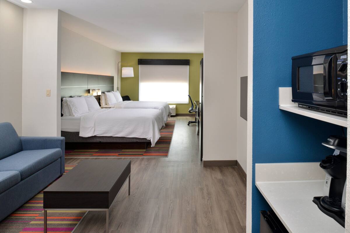 A hotel room with a bed, a blue sofa, a coffee table, a microwave, and a TV.