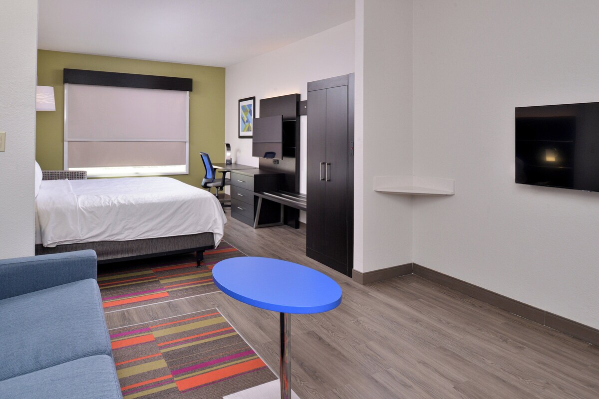 Ein Hotelzimmer mit einem Bett, einem Schreibtisch, einem Sessel, einem Fernseher und einem kleinen Tisch.