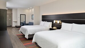 A hotel room with two beds, a desk, a chair, a nightstand with a phone, and a colorful striped rug.