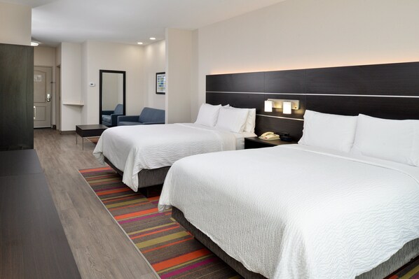 Ein Hotelzimmer mit zwei Betten, einem Schreibtisch, einem Stuhl, einem Nachttisch mit Telefon und einem farbenfrohen Streifen Teppich.