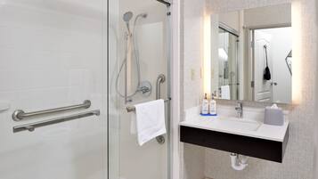 A modern bathroom with a glass shower enclosure, a white sink with a black countertop, and a mirror with a geometric tile backsplash.