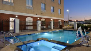 A swimming pool with a metal ladder and a fence, surrounded by a brick building with multiple windows and a door.