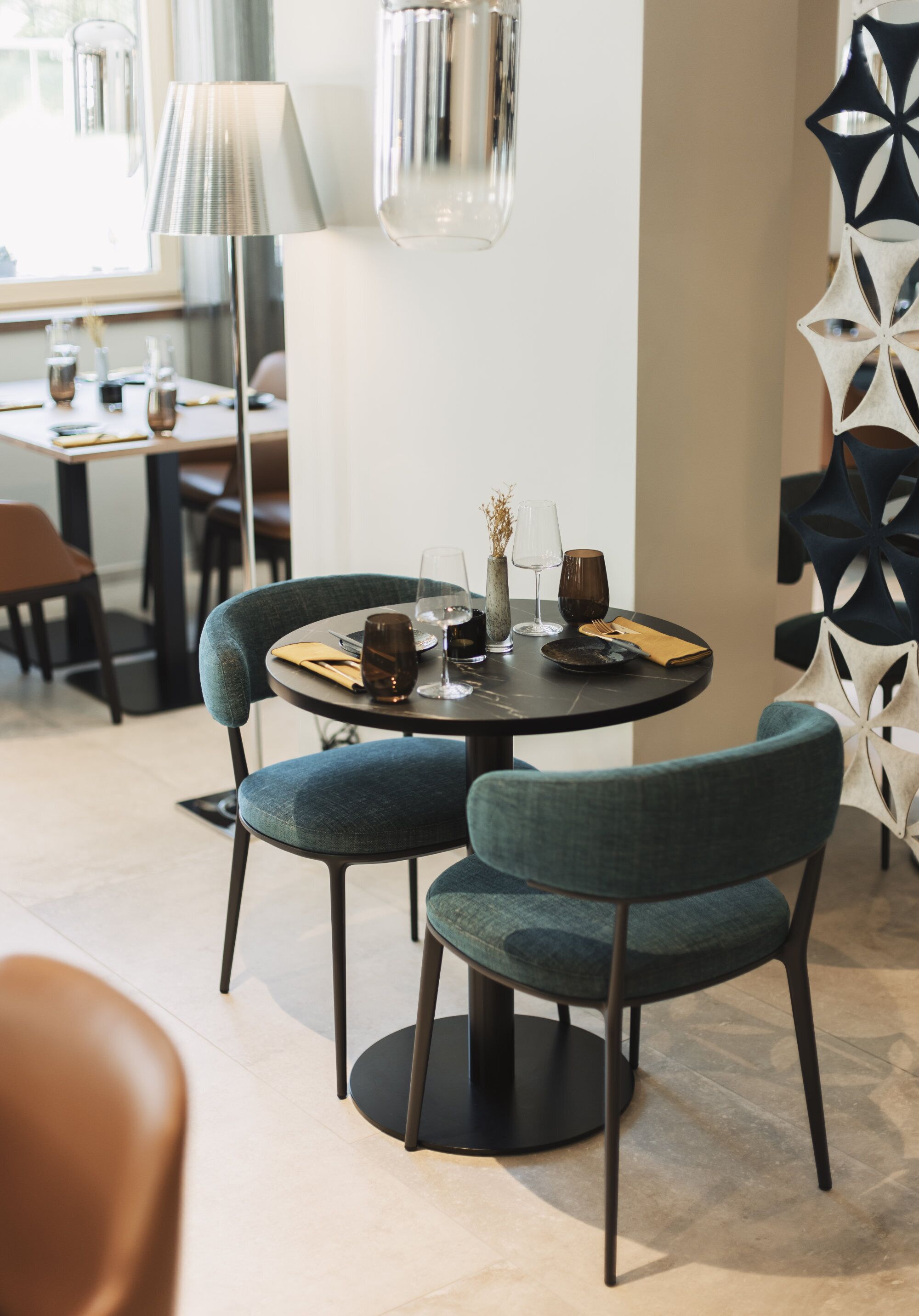 A dining area with a round table, two upholstered chairs, a lamp, and a decorative wall piece.