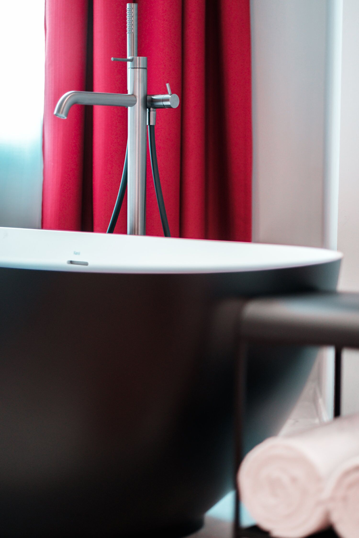 A modern bathroom with a bathtub, a showerhead, and a towel on a chair.