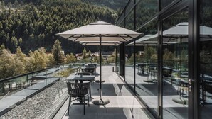 A terrace with outdoor seating, glass railings, and a view of a forested mountain range. - AlpenParks The Secret Sölden (Soelden)