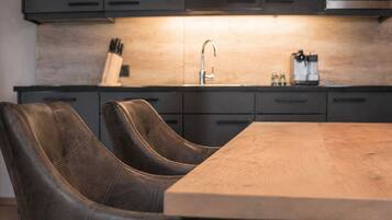 A modern kitchen with dark cabinets, a wooden dining table, and two leather chairs.