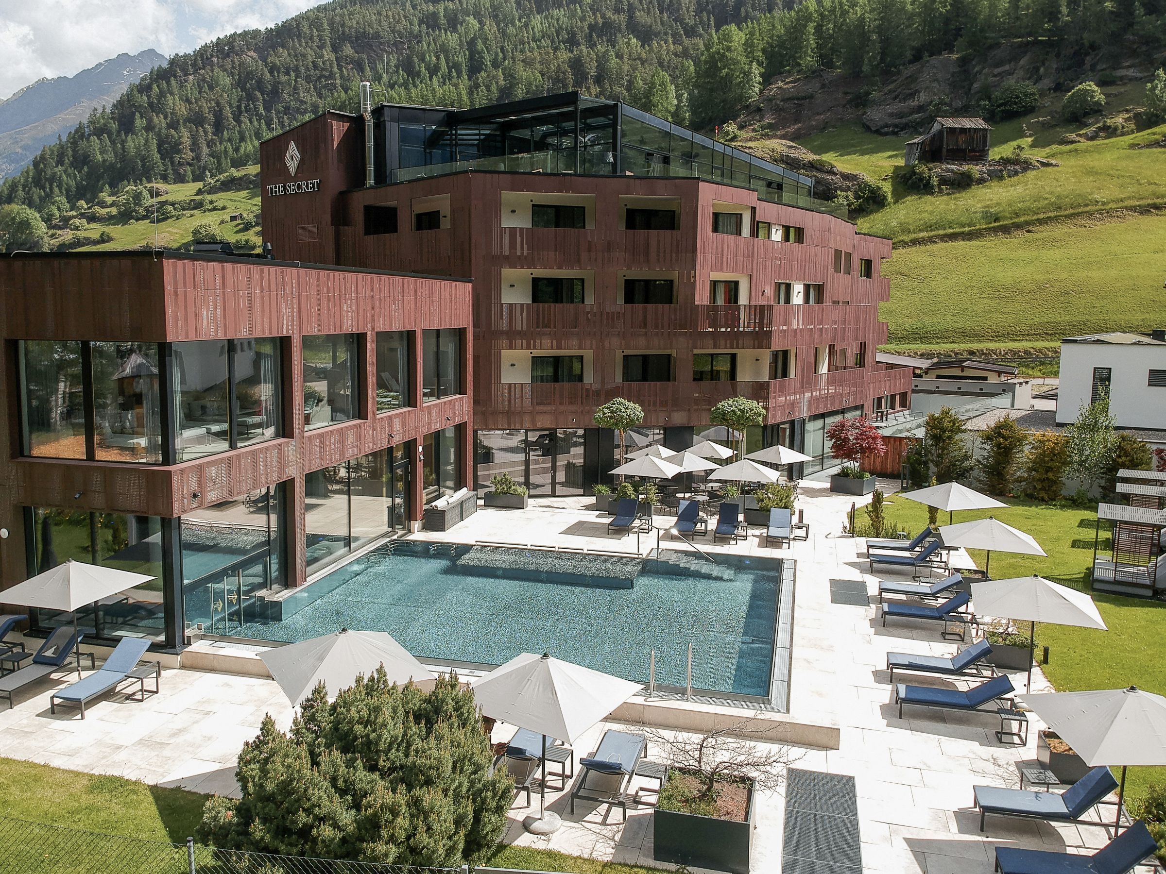 A modern hotel with a pool area, lounge chairs, and a view of the surrounding landscape.