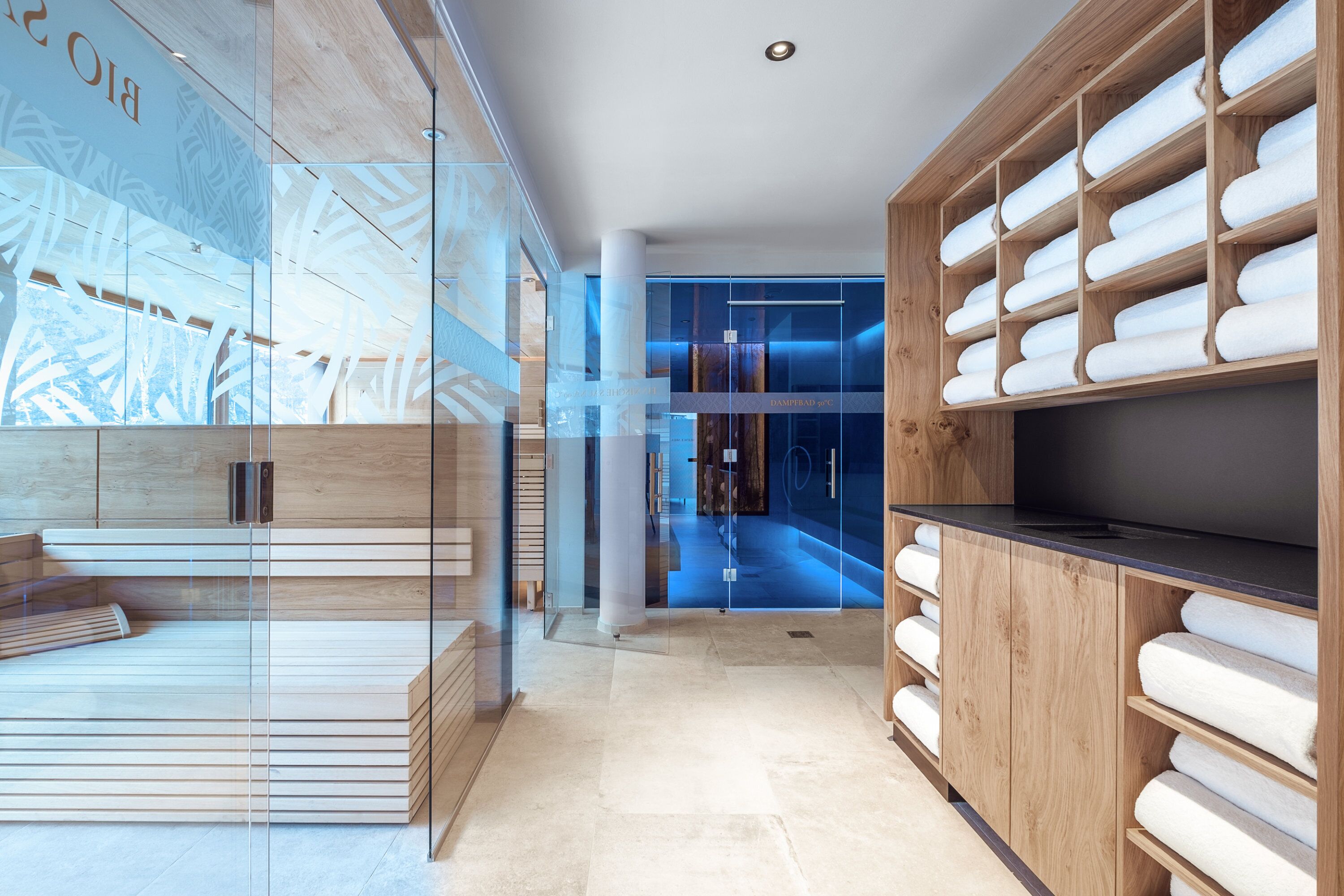 Un moderno vestíbulo de hotel con un muro de cristal, asientos de madera y una gran estantería de madera con toallas.