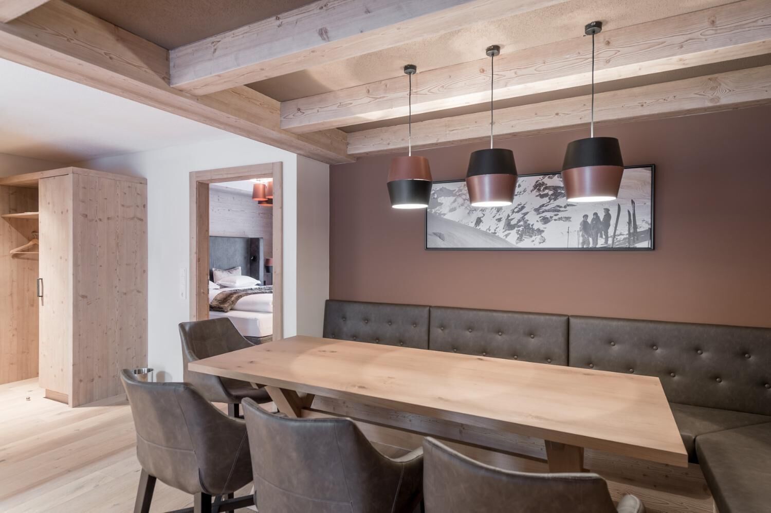 A dining area with a long wooden table, cushioned bench seating, and pendant lighting.
