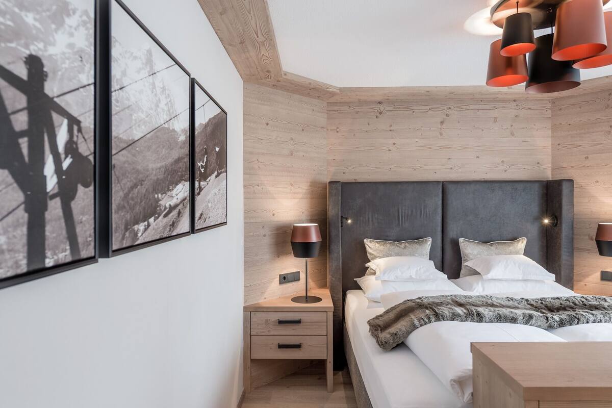A modern bedroom with a wooden headboard, a bed with white linens, two bedside tables with lamps, and framed photographs on the wall.