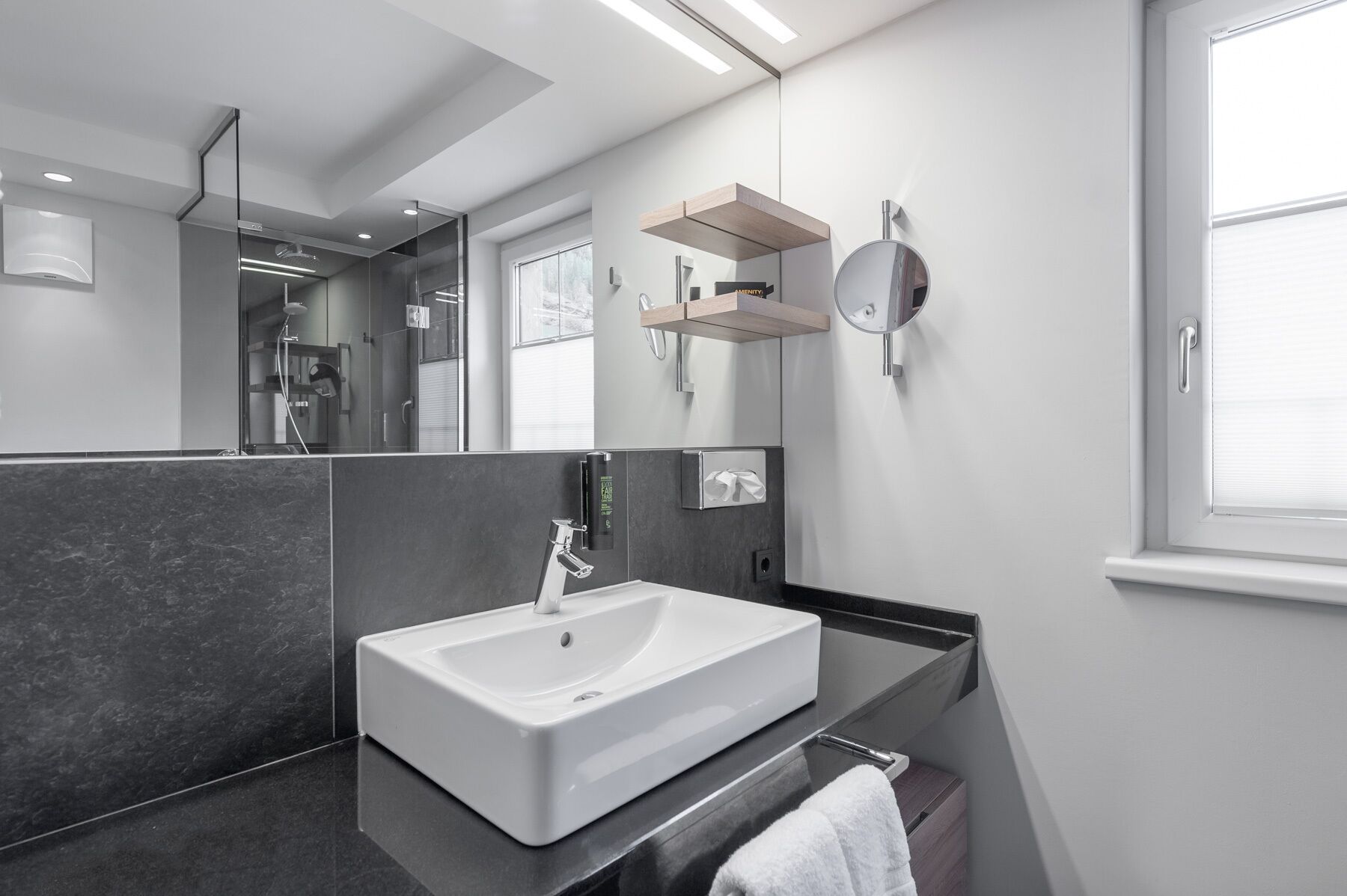 A modern bathroom with a large mirror, a white sink, and a towel rack.