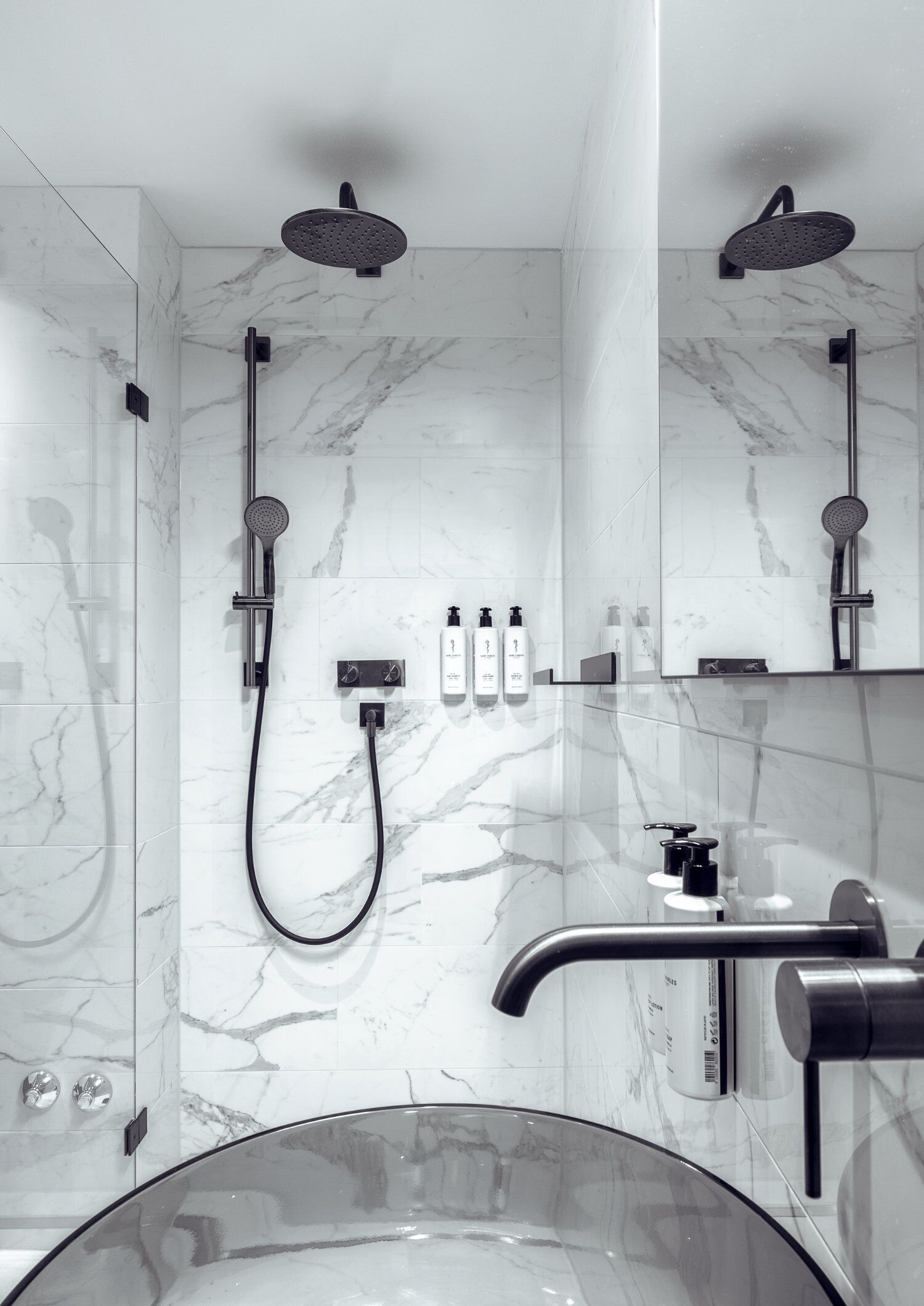 Une salle de bain moderne dotée d’une baignoire entourée de parois en verre, de deux douches et d’un meuble-lavabo avec un évier et un miroir.