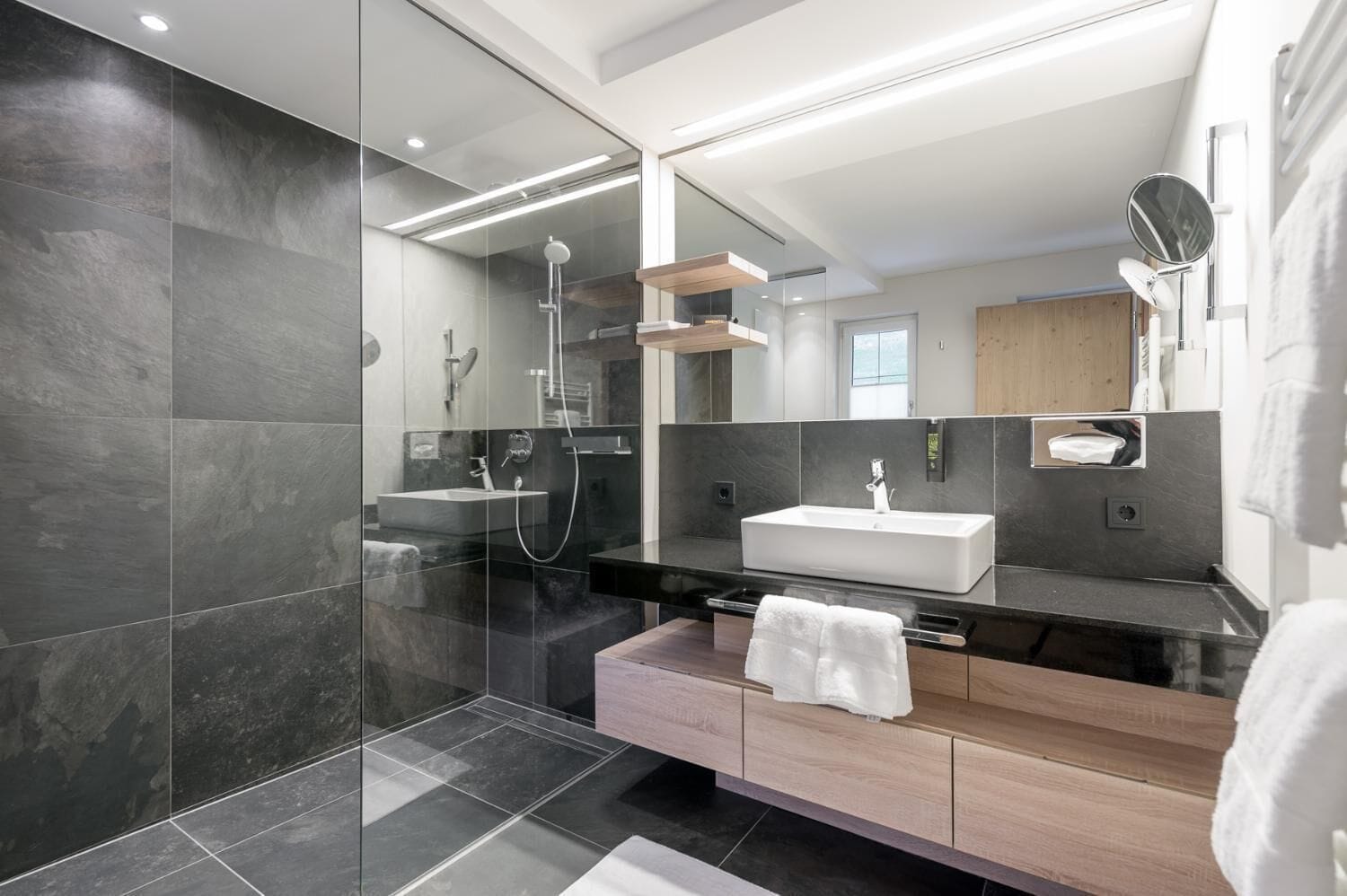 Un baño moderno con cabina de ducha de vidrio, un espejo grande y un mueble de tocador de madera.