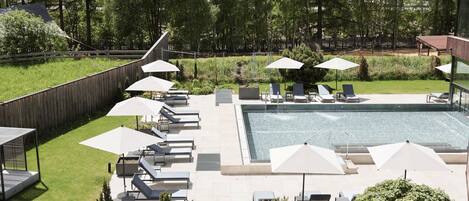 A rooftop pool area with lounge chairs and umbrellas, surrounded by a wooden fence and greenery.