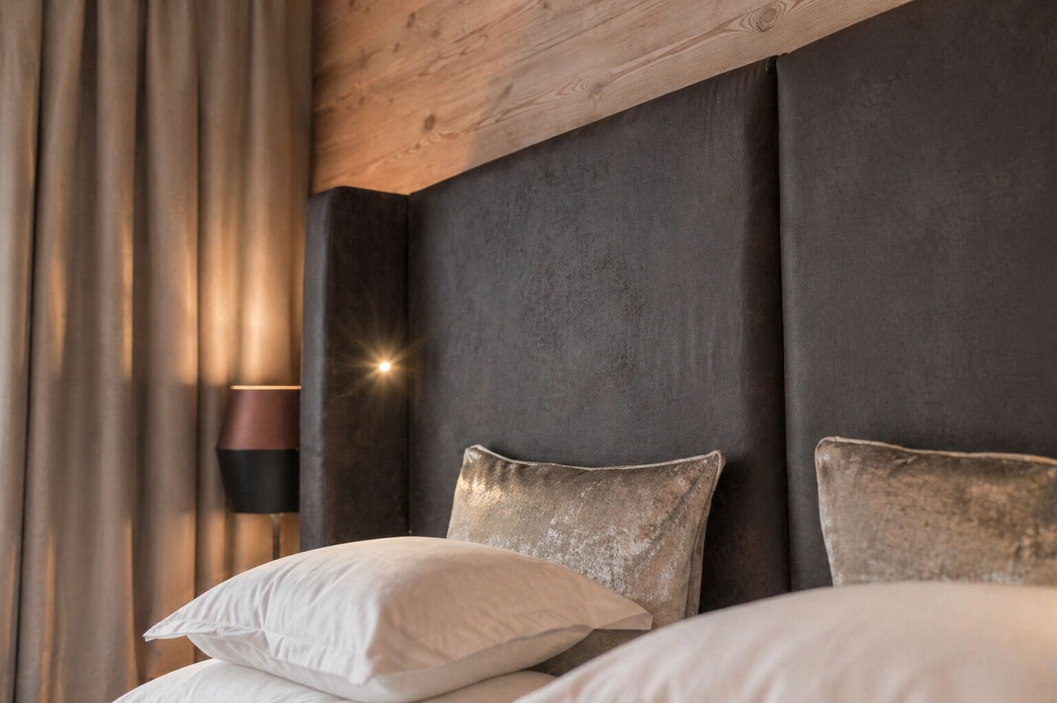 Ein Schlafzimmer mit dunklem Kopfteil, einer Nachttischlampe und einem Fenster mit Vorhängen.