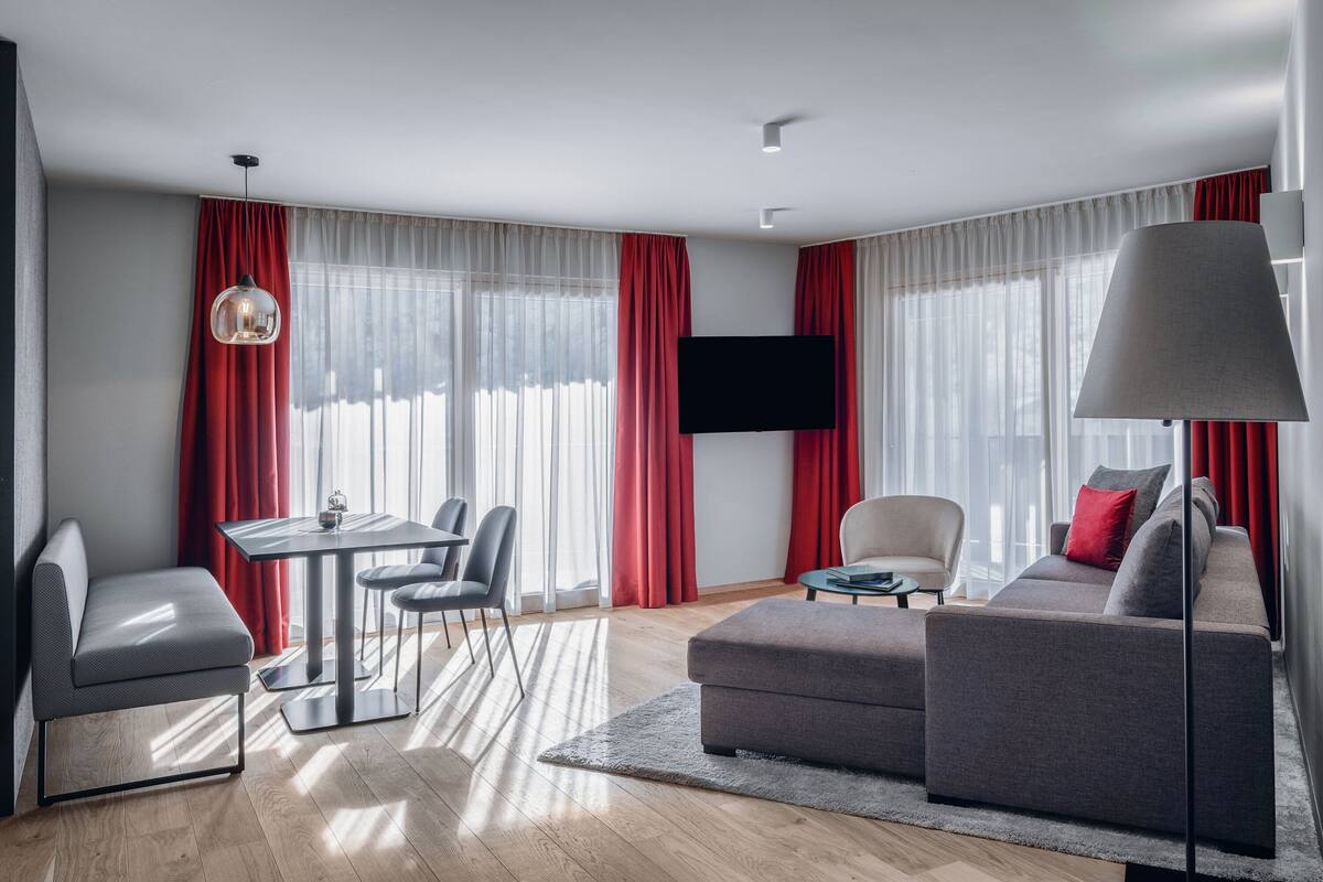 A modern living room with a sofa, a dining table with chairs, a TV mounted on the wall, and a lamp.