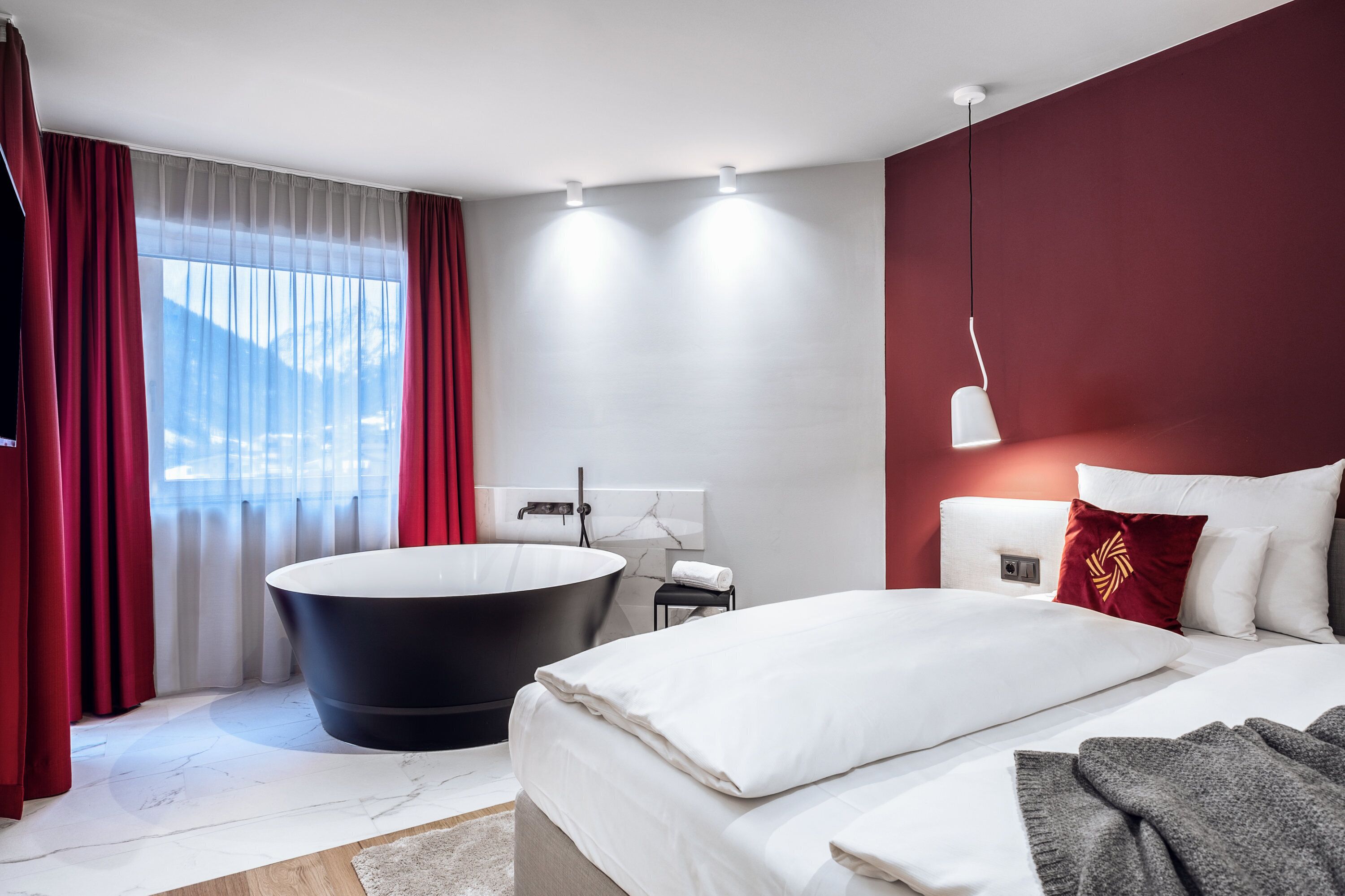 Quarto de hotel moderno com uma cama grande, uma banheira preta e vista para as montanhas pela janela.