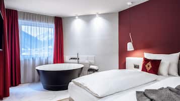 Quarto de hotel moderno com uma cama grande, uma banheira preta e vista para as montanhas pela janela.