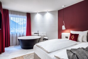 A modern hotel room with a large bed, a black bathtub, and a view of mountains through the window. - AlpenParks The Secret Sölden (Soelden)