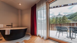 A modern bathroom with a freestanding bathtub, a marble-tiled wall, and a view of a balcony with outdoor furniture. - AlpenParks The Secret Sölden (Soelden)