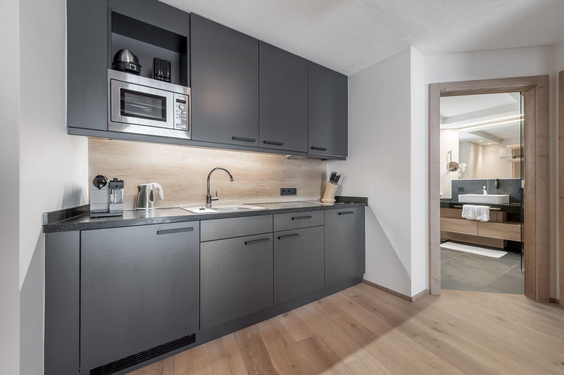 A modern kitchen with dark cabinets, a stainless steel oven, a coffee machine, and a sink.