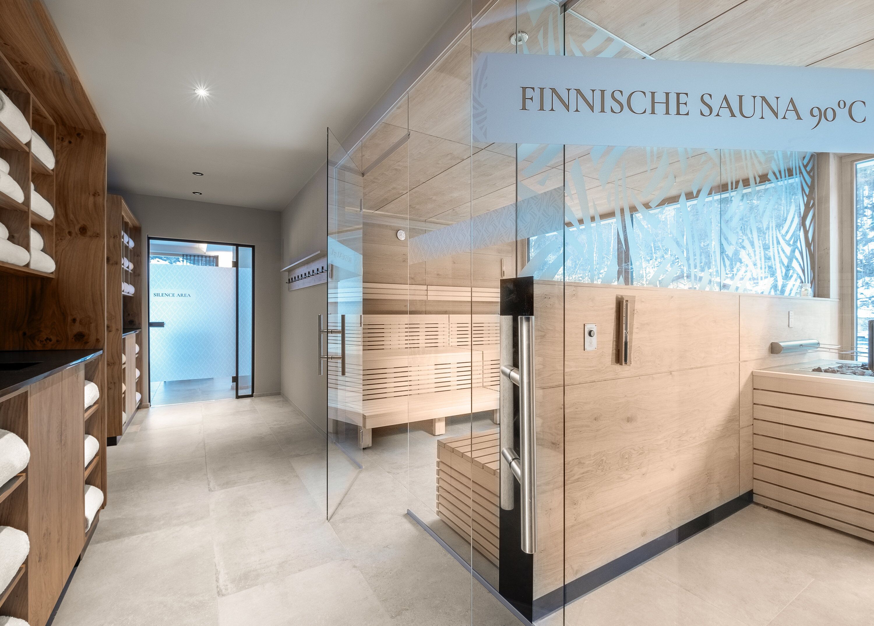 A modern sauna room with glass walls, wooden benches, and a sign indicating a 90°C temperature.