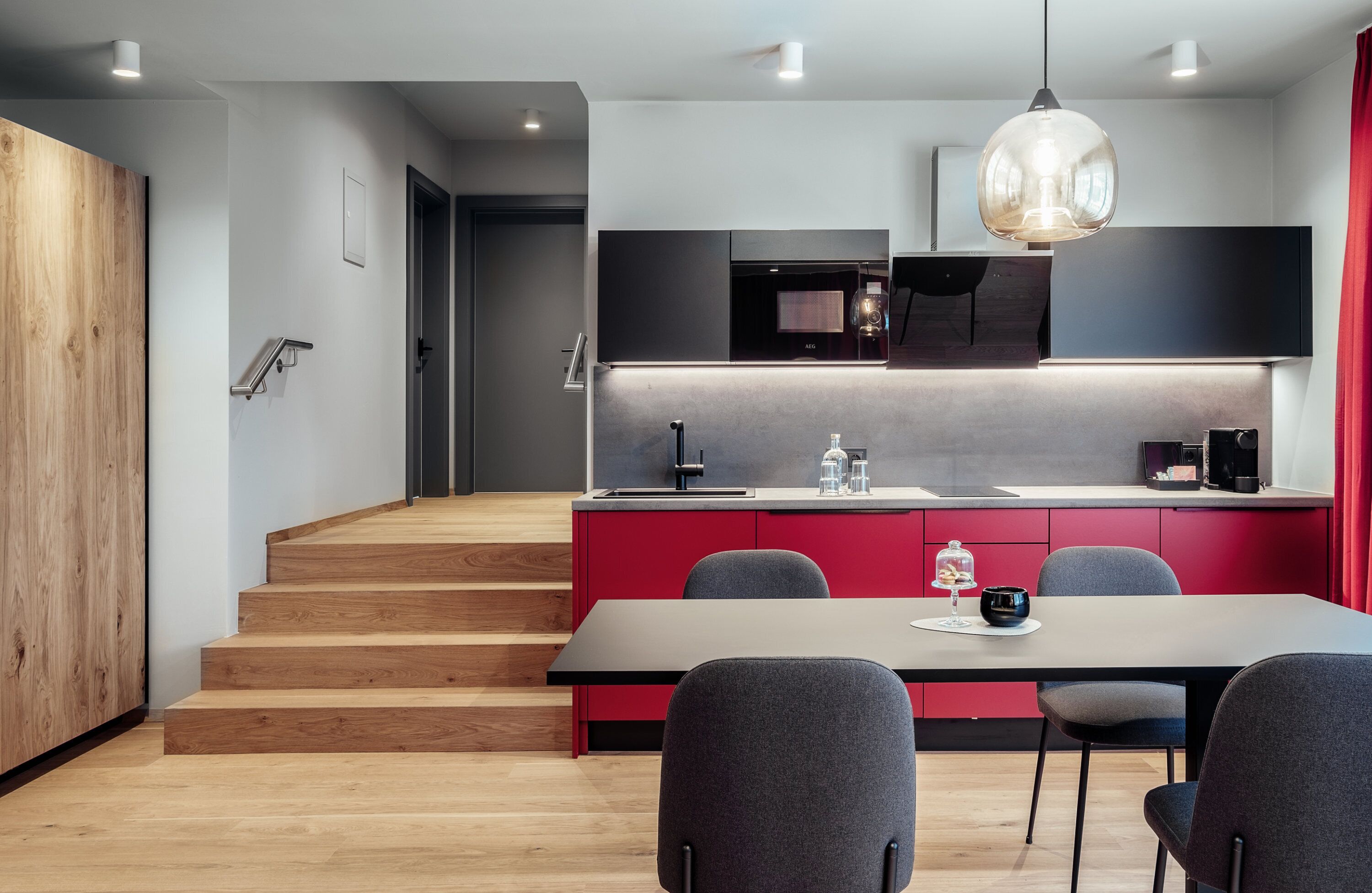 Une cuisine moderne avec un escalier en bois, un coin repas avec une table et des chaises, et un mur d’accent de couleur rouge.