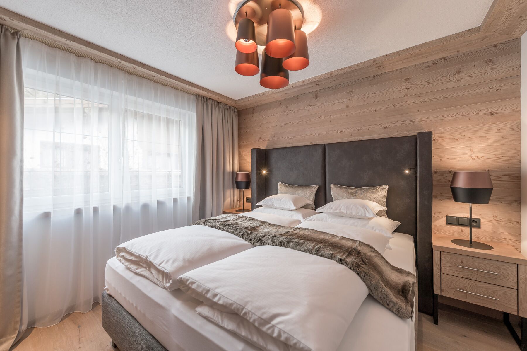 A modern bedroom with a large bed, wooden headboard, and a nightstand with a lamp.
