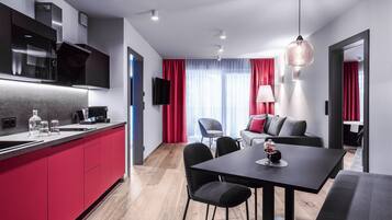 A modern kitchen with red cabinets, a dining area with a black table, and a living room with a gray sofa.