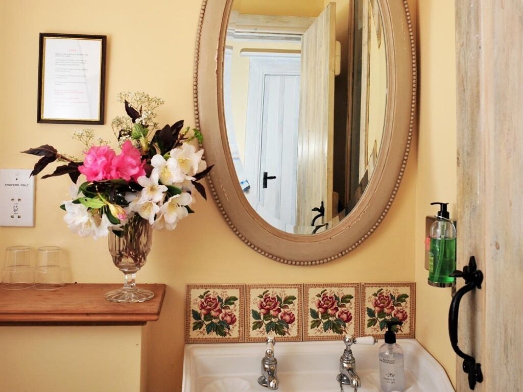 Une salle de bain avec un miroir, un vase de fleurs, un lavabo et une porte en arrière-plan.
