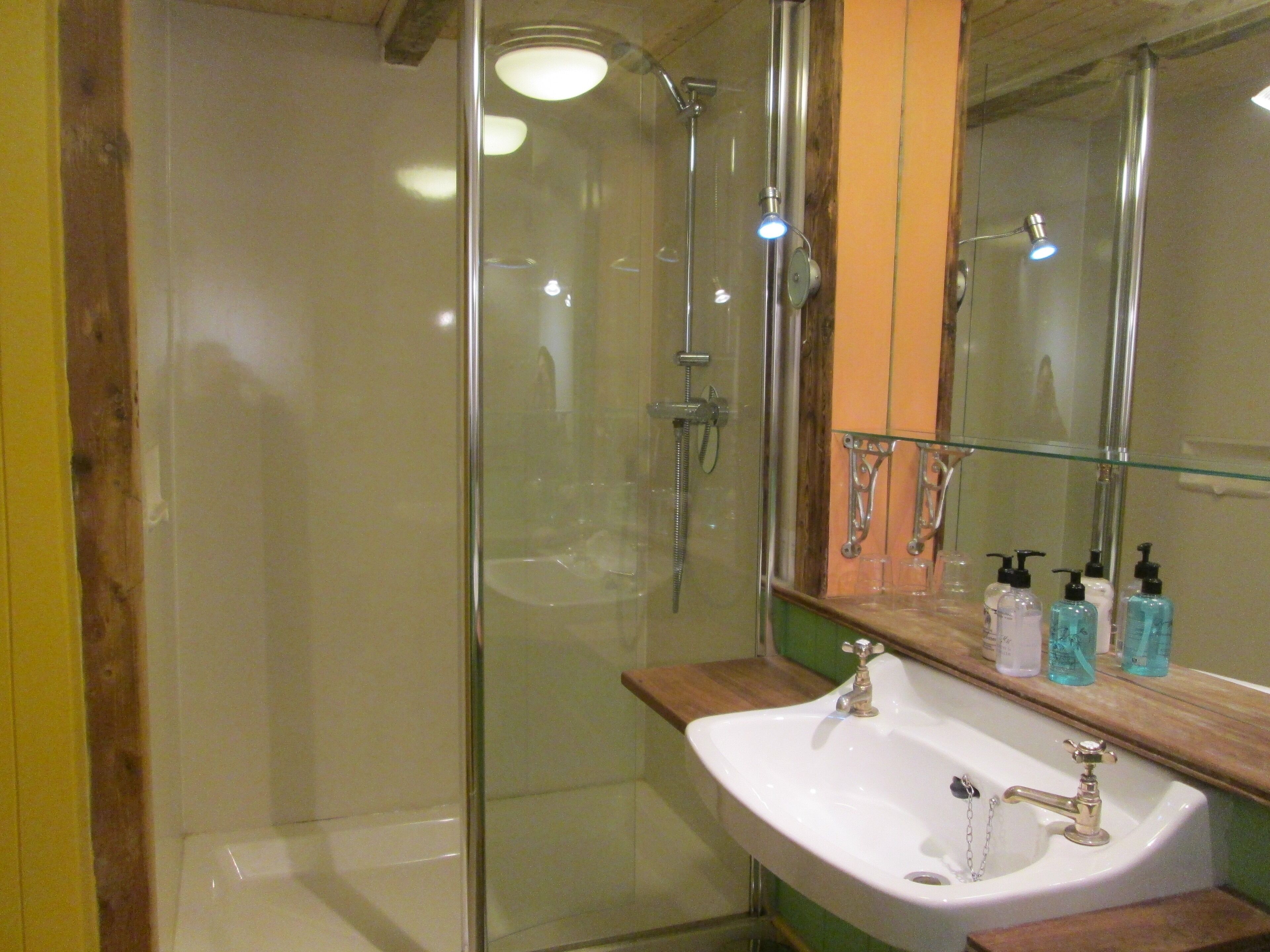 Un baño con ducha envuelta en vidrio, un lavamanos blanco y un espejo sobre él.