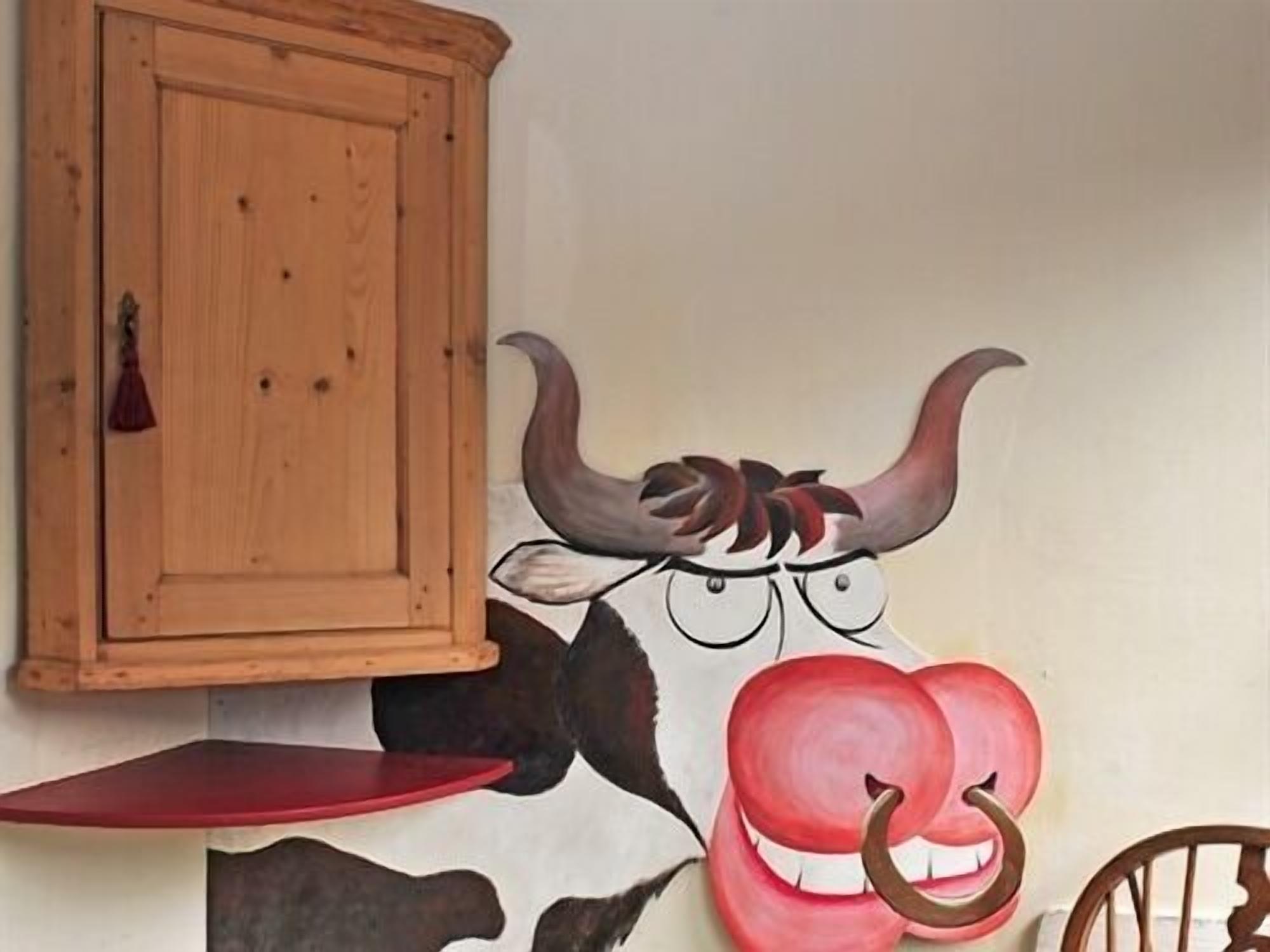 A wall with a bull mural, a wooden cabinet, and a red chair.