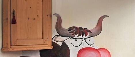 A wall with a bull mural, a wooden cabinet, and a red chair.