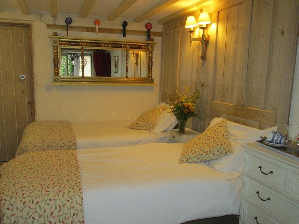 A room with two beds, a wooden ceiling, a mirror, a wall-mounted lamp, and a dresser.