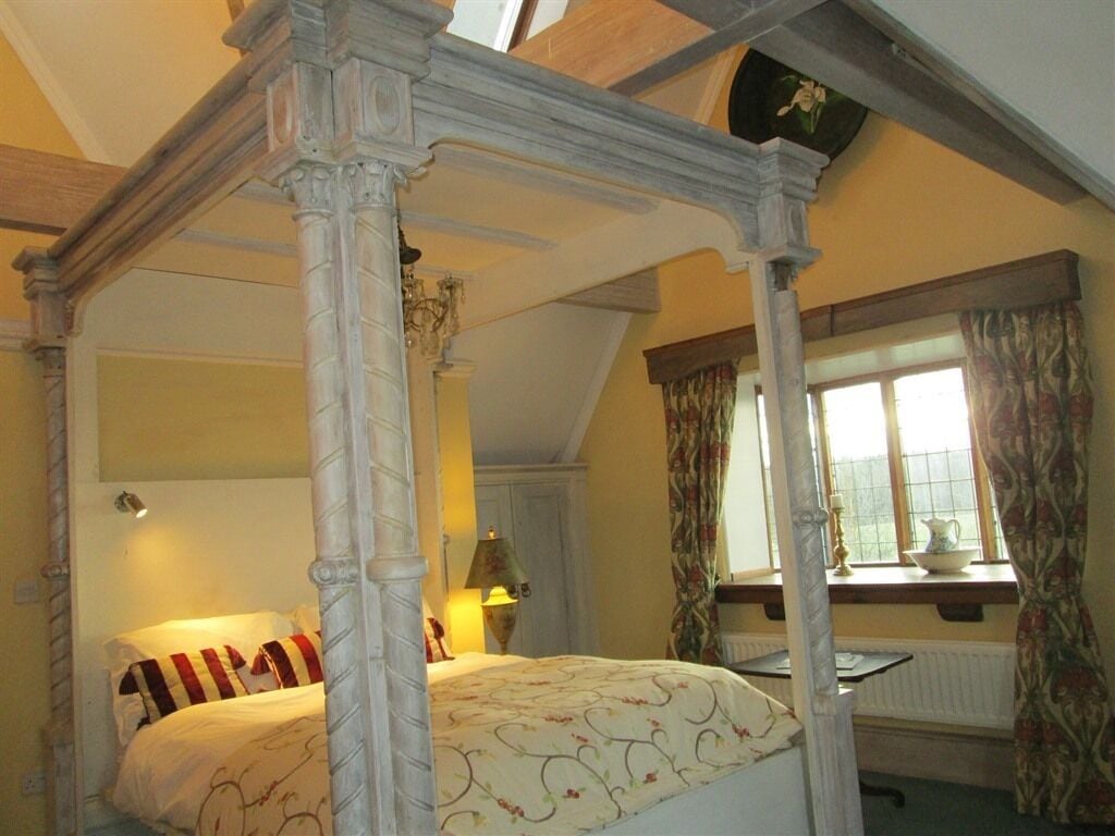 A four-poster bed with a floral bedspread, a window with curtains, and a radiator below.