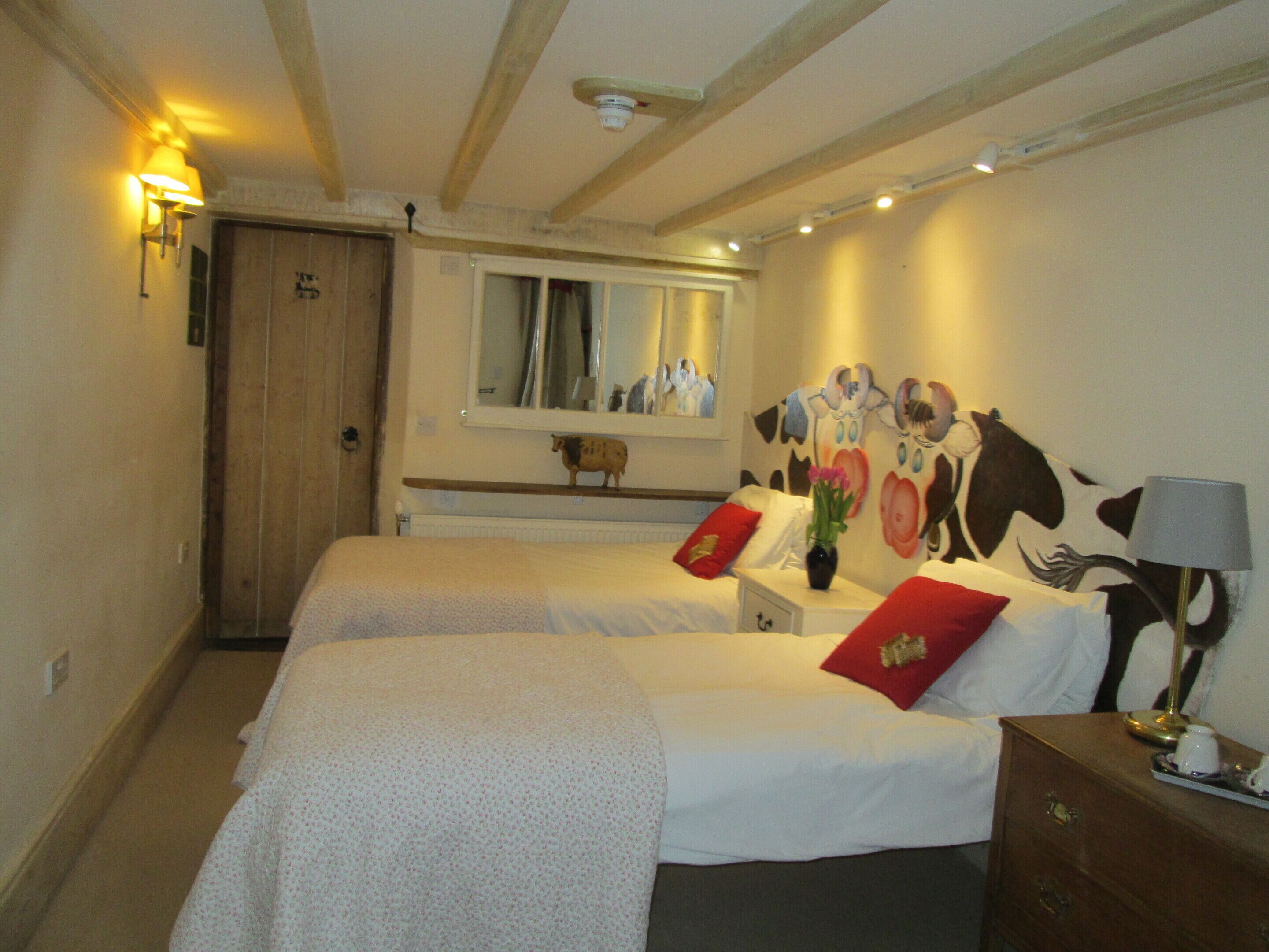 Habitación de hotel con dos camas, techo de madera, ventana con vistas y un cuadro de vaca en la pared.