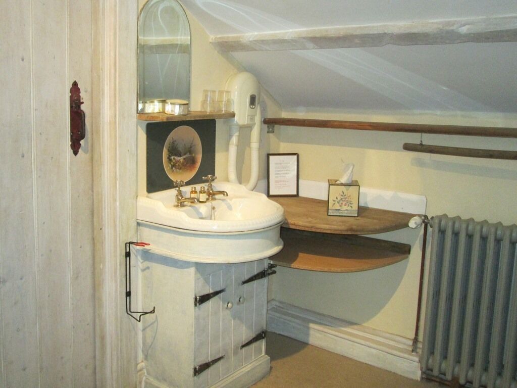 A compact bathroom with a white sink, a mirror, and a wooden shelf above it.